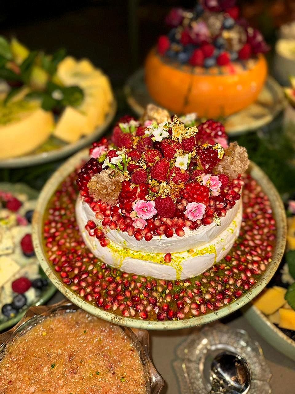 Bolo decorado com romã, framboesas e flores comestíveis